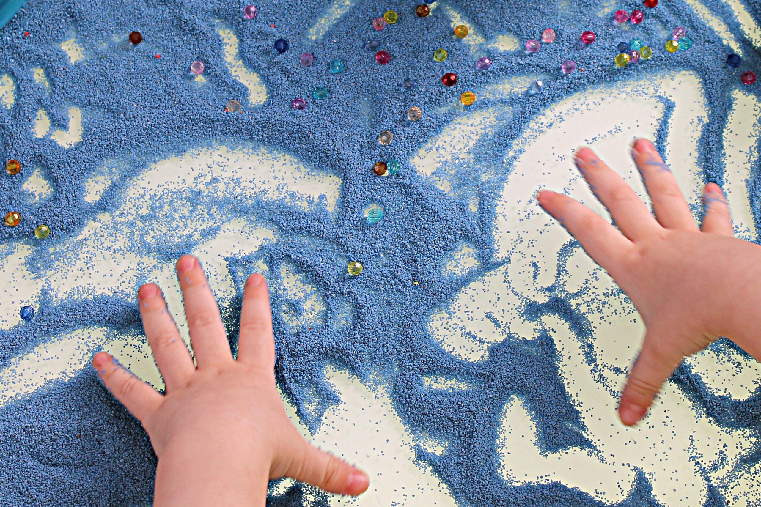 sand therapy, child's hands are painted on a white table with blue sand